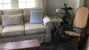 Un salón acogedor con un sofá color beige, una mesa de centro de madera, un sillón de mimbre y una mesita con una planta y una vela.