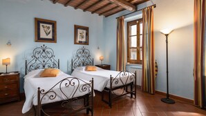 Una habitación con dos camas, una mesita de noche, una lámpara de pie y una ventana con cortinas.