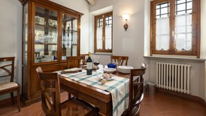 Un comedor con una mesa de madera, sillas, un armario con puertas de cristal y una ventana con cortinas.