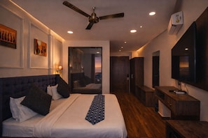 Habitación de hotel moderna con una cama grande, ventilador de techo, televisión y vista a la ciudad.