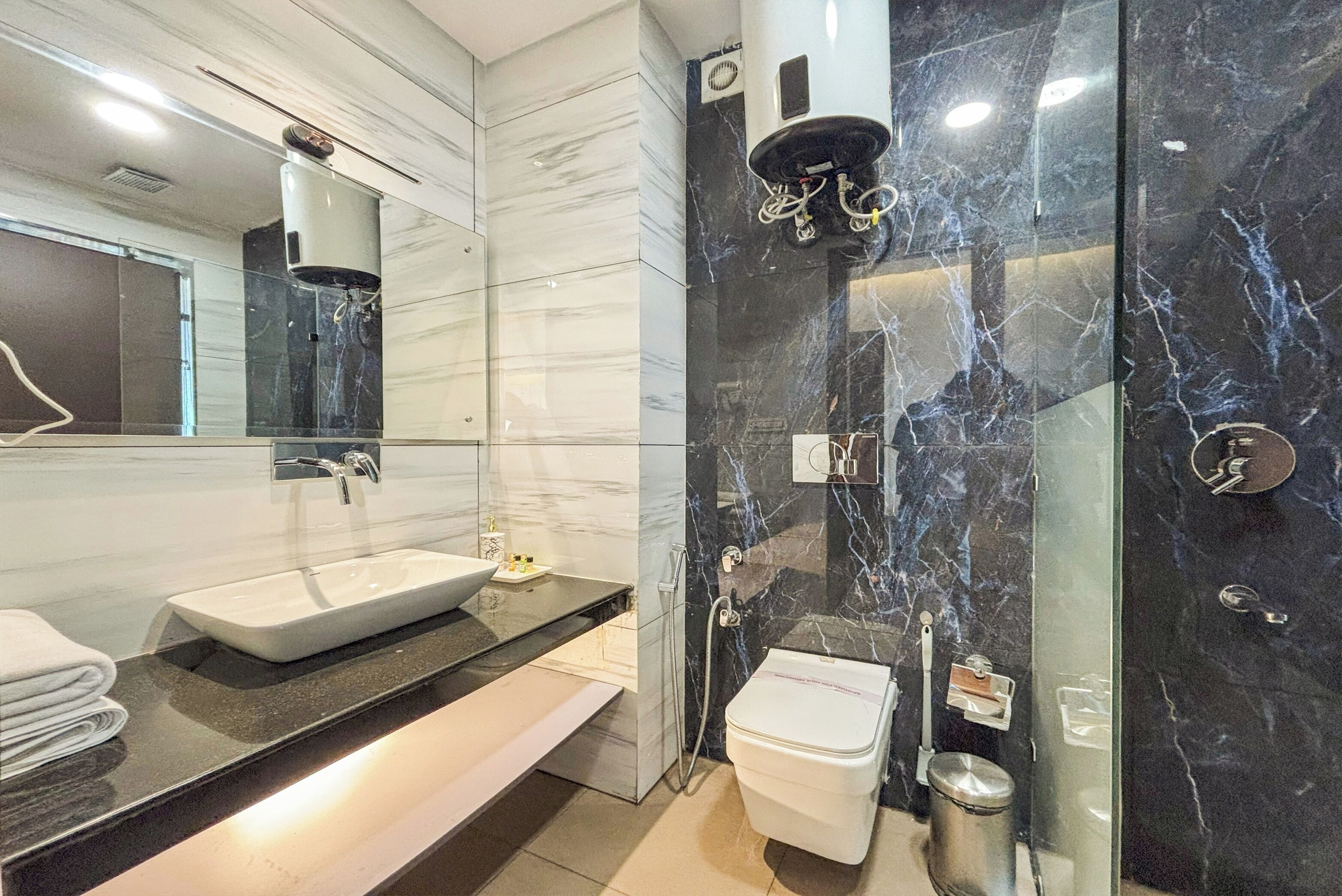 A modern bathroom with a large mirror, a white sink, a toilet, and a glass-enclosed shower.