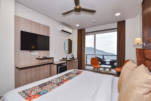 Habitación de hotel con cama, escritorio, televisión, espejo, ventana con vistas y ventilador de techo.