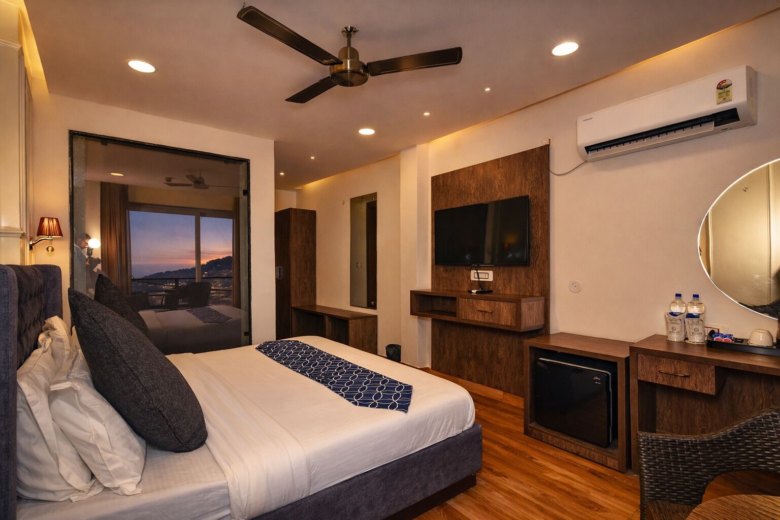 Una habitación de hotel moderna con cama, escritorio, televisor y un amplio ventanal con vistas a la ciudad.