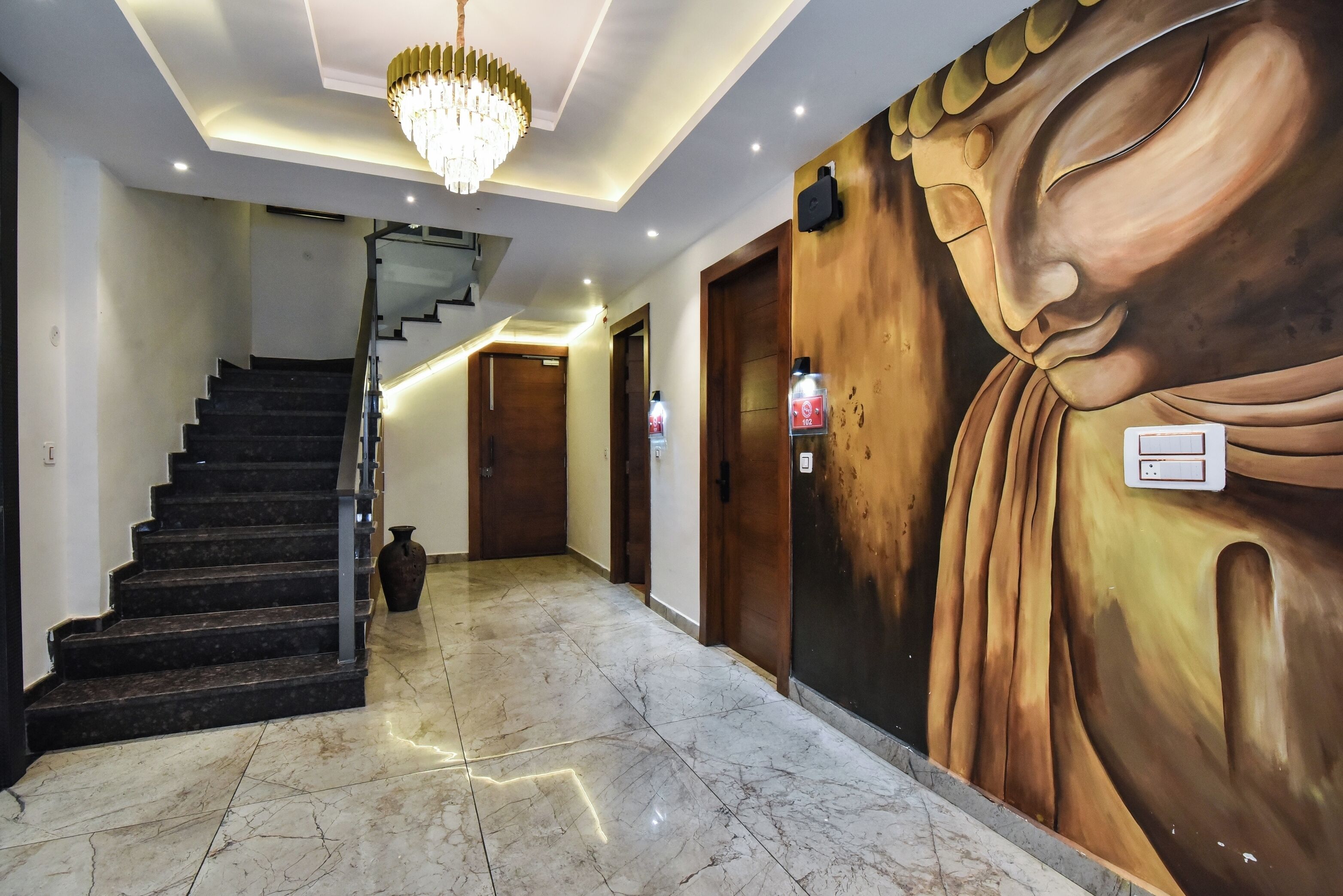 A hallway with marble flooring, a staircase, a chandelier, and a large Buddha mural.