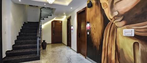 A hallway with marble flooring, a staircase, a chandelier, and a large Buddha mural.