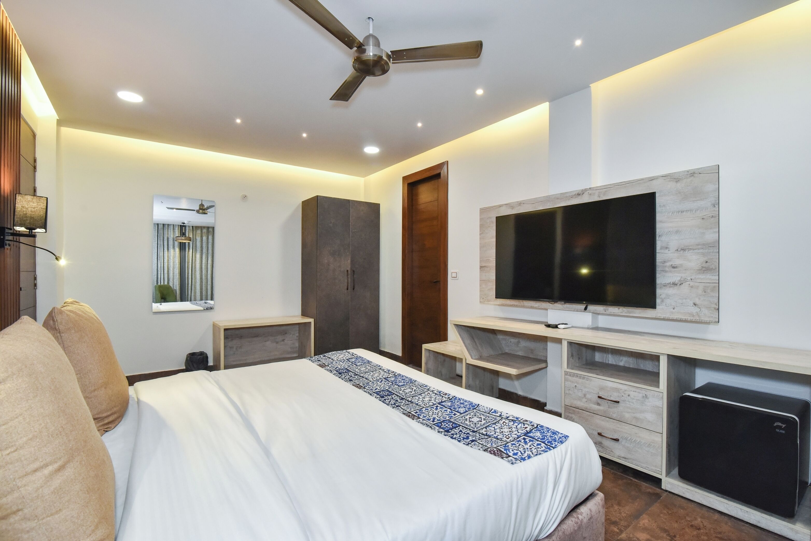 A modern bedroom with a bed, a TV, a ceiling fan, and a desk.