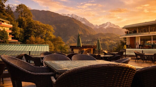 Une terrasse dotée de meubles et de tables en osier, offrant une vue sur un paysage montagneux, avec un bâtiment abritant un restaurant en arrière-plan.