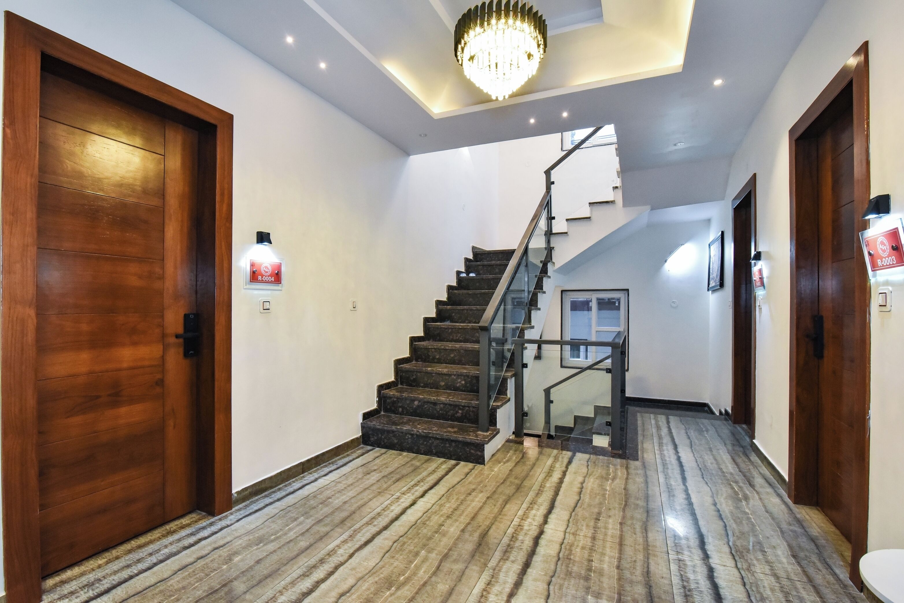 Un interior moderno con una puerta de madera, una escalera con barandilla de vidrio y un candelabro.
