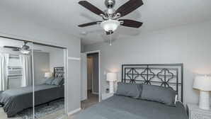 Quarto com cama, ventilador de teto, mesa de cabeceira com abajur e espelho.