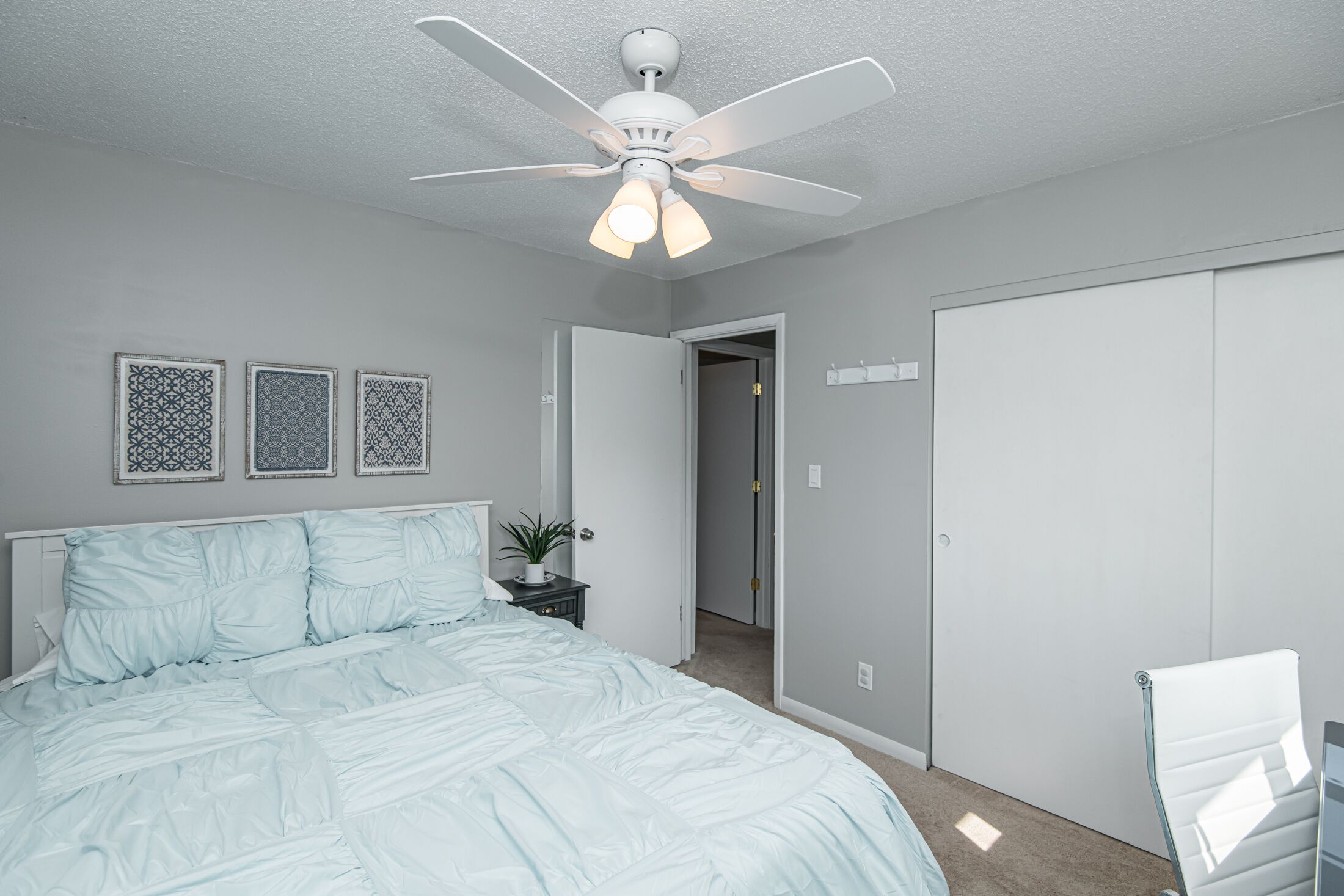 A bedroom with a bed, a ceiling fan, a door, and a wall-mounted light switch.