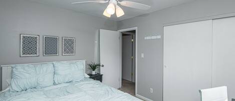 A bedroom with a bed, a ceiling fan, a door, and a wall-mounted light switch.
