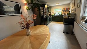 A modern kitchen with a curved wooden table, a refrigerator, and a potted plant. - Dreamy 3BD House W/large Patio - Stoke Newington! (London)