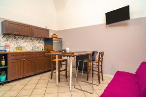 Una cocina compacta con armarios de madera, salpicadero de azulejos, horno empotrado y una zona de comedor con dos sillas.