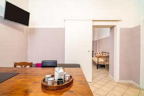 A dining area with a wooden table, chairs, a coffee tray, and a television mounted on the wall.
