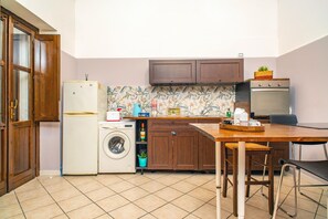 Cocina compacta con lavadora, refrigerador, armarios de madera y un comedor con mesa y sillas.
