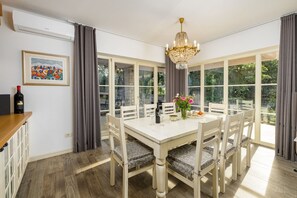 Uma área de refeições com uma mesa, cadeiras, um lustre, uma garrafa de vinho e um quadro na parede.