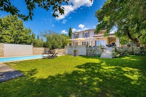 A residential property with a swimming pool, a well-maintained lawn, and a stone wall.