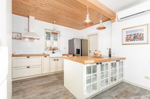 A kitchen with wooden cabinets, a central island, pendant lights, and a refrigerator. - Villa Ardiletta by Villsy (Rakovci)