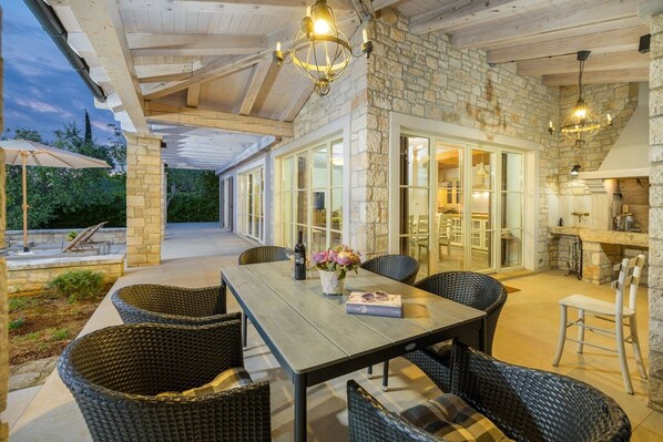 An outdoor patio with a dining table, wicker chairs, stone walls, and a stone fireplace.