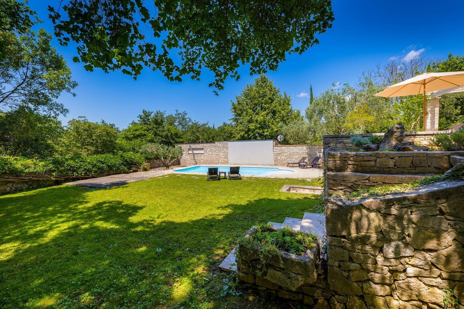 A backyard with a swimming pool, stone steps, and a stone wall.