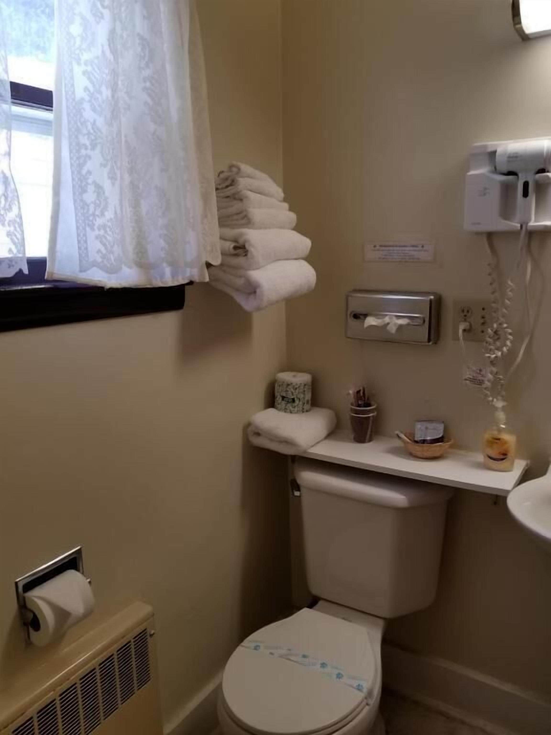 Un baño pequeño con inodoro, dispensador de toallas de papel, secamanos y ventana con cortina.