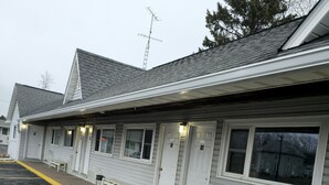 A motel with a row of rooms, each with a door and windows, and a parking lot with yellow lines. - Home Motel Abbotsford (Abbotsford)