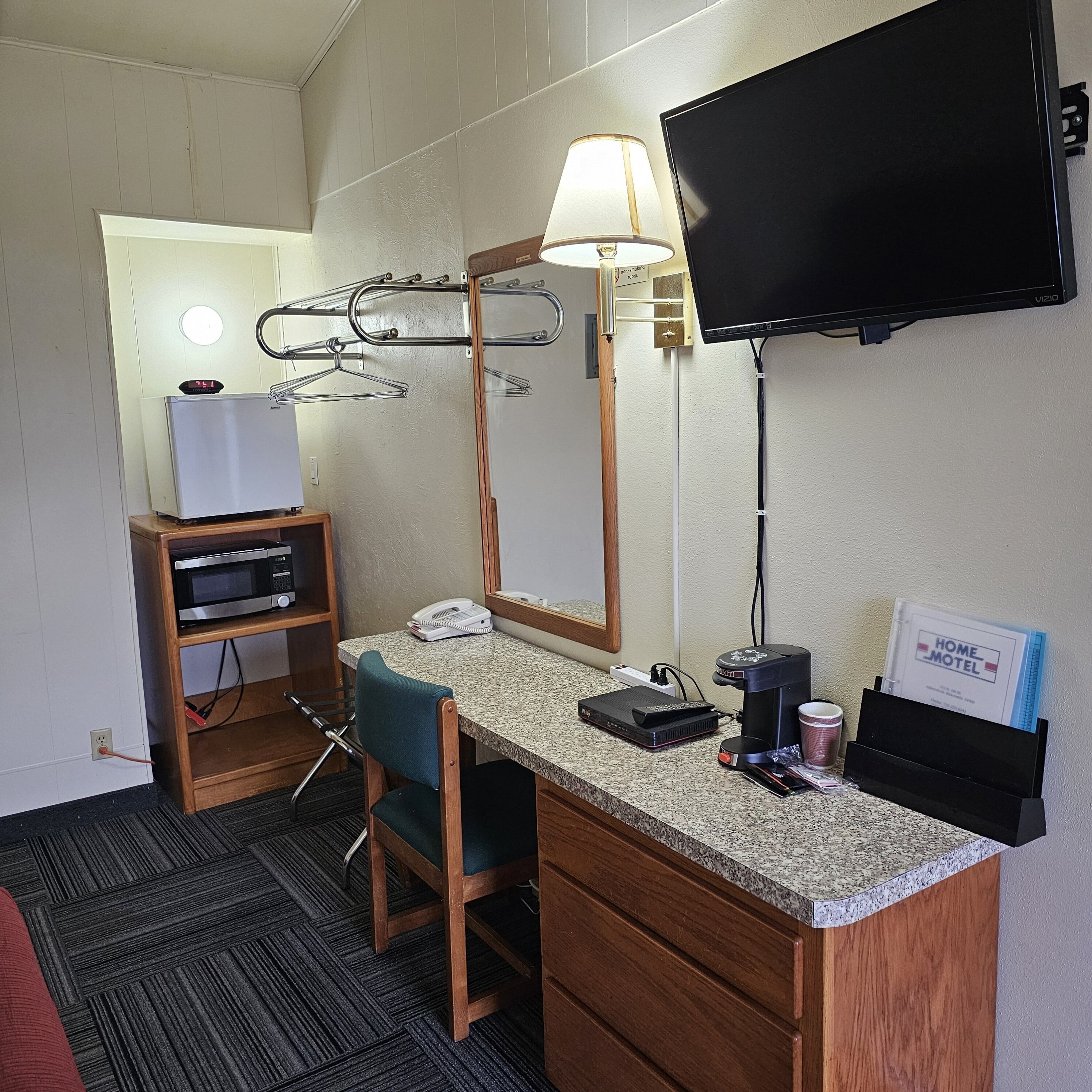 A hotel room with a desk, chair, TV, lamp, and a wall-mounted drying rack.