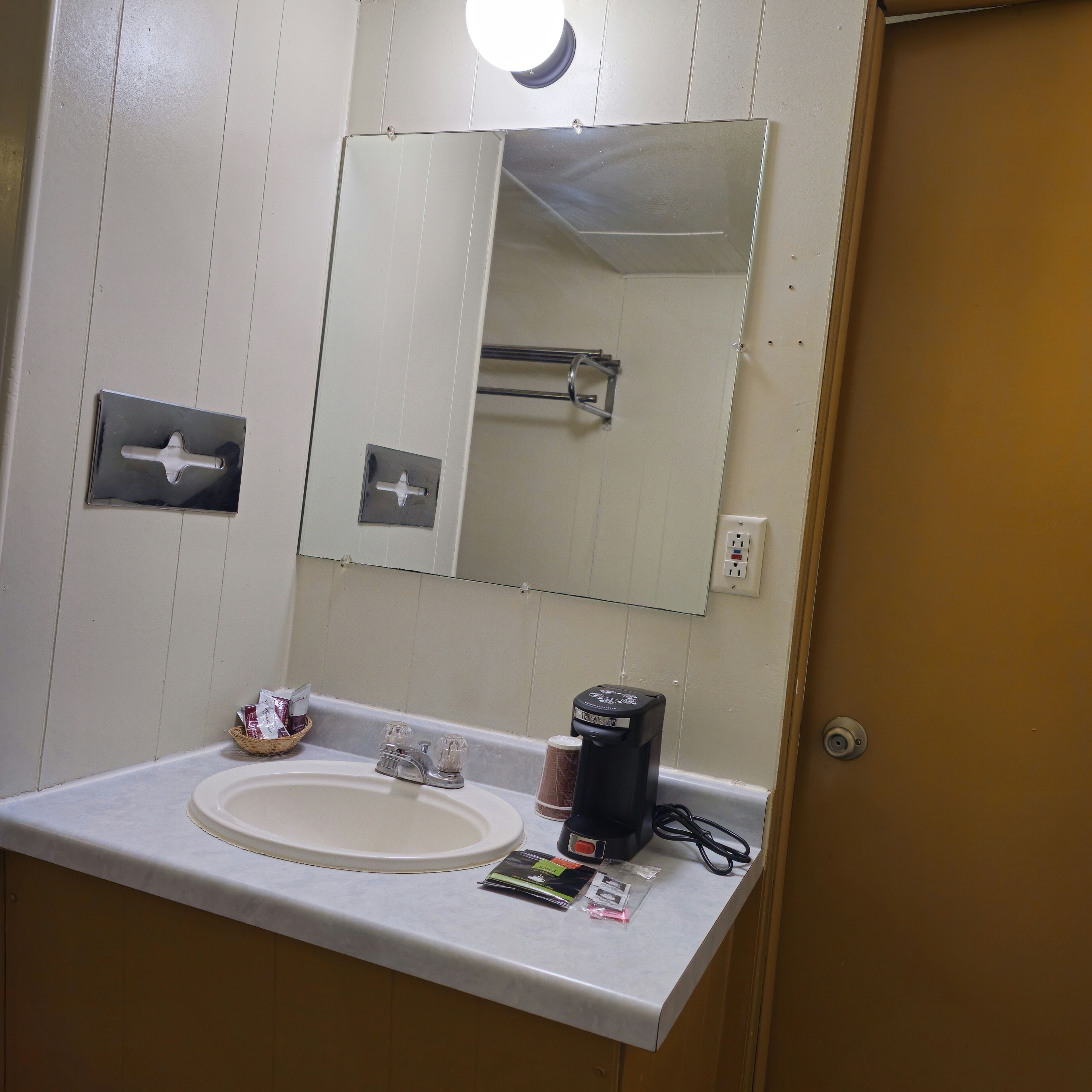 Un baño con lavamanos blanco, espejo, perchero y cafetera.