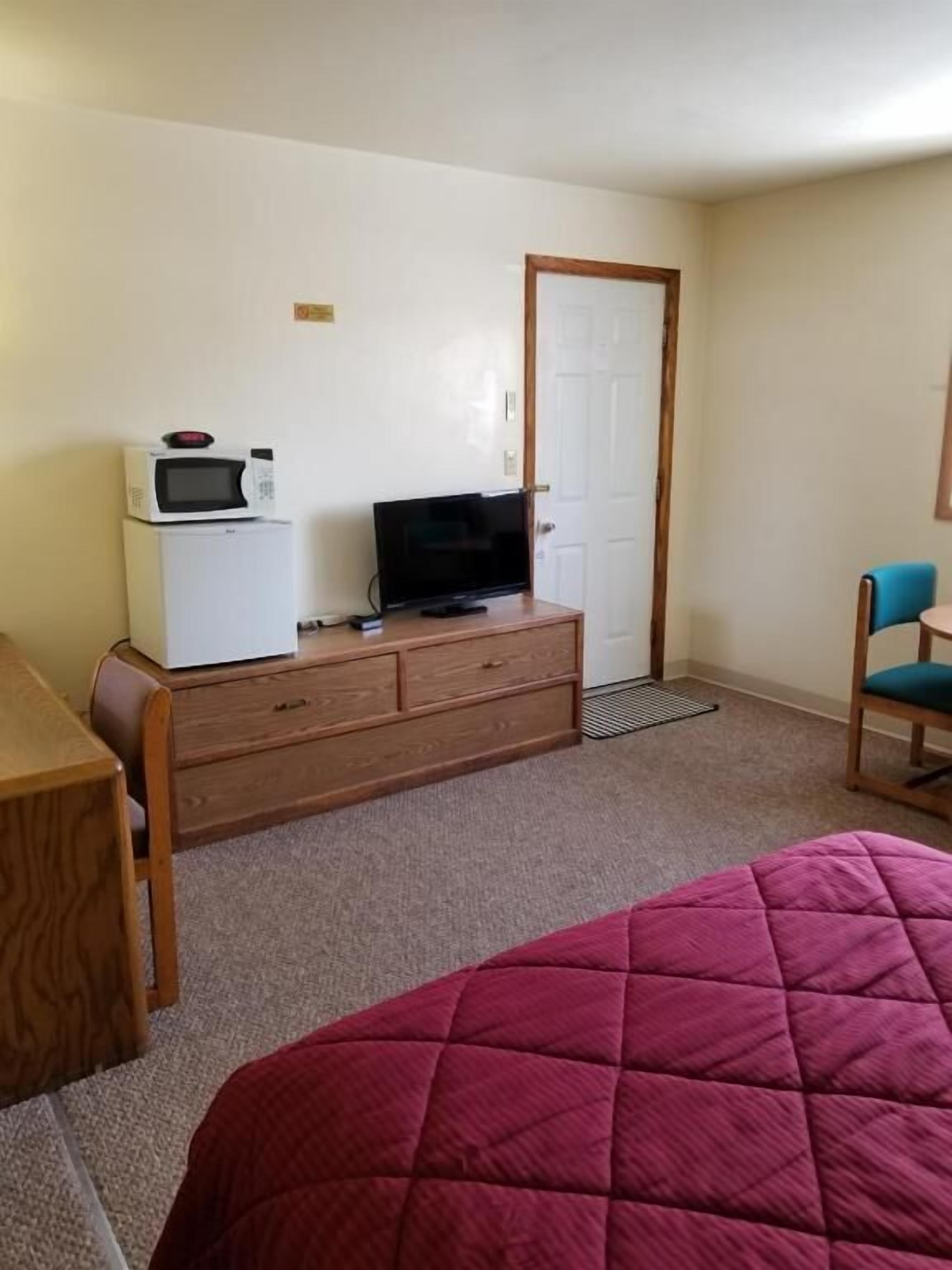 Una habitación de hotel con cama, cómoda de madera con microondas y televisión, escritorio y silla.