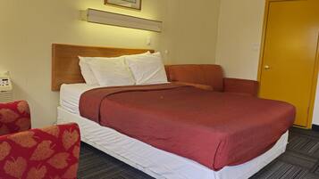 A hotel room with a bed, a wooden headboard, a ceiling fan, a framed picture on the wall, and a door.