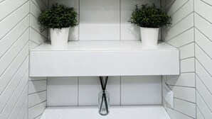 Een badkamer met witte betegelde wanden, twee witte planken en een klein decoratief object op de bovenste plank.