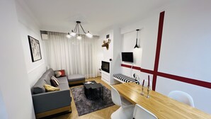 Een moderne woonkamer met een grijze bank, een houten eettafel en een aan de muur bevestigde televisie.