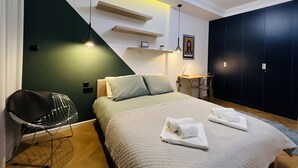 Een moderne slaapkamer met een bed, een stoel, een bureau en een donkere garderobe.