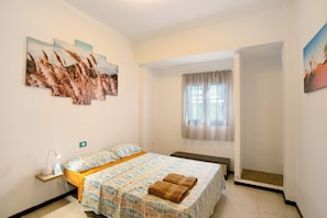 Un dormitorio con cama, una mesita de noche con lámpara, una ventana con cortinas y decoración en la pared.