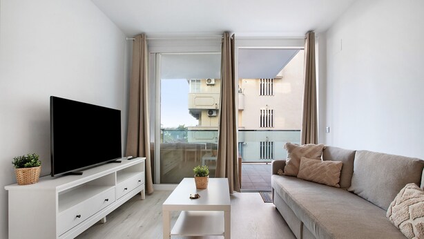 Ein modernes Wohnzimmer mit Flachbildfernseher, einem weißen Couchtisch, einem beigefarbenen Sofa und einem Balkon mit Vorhängen.