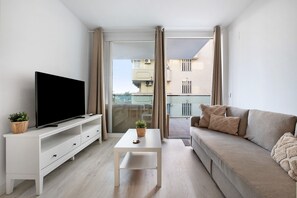 A modern living room with a flat-screen TV, a white coffee table, a beige sofa, and a balcony with curtains. - Apartment "Edificio Italia" with Private Terrace & Wi-Fi (Benalmadena)
