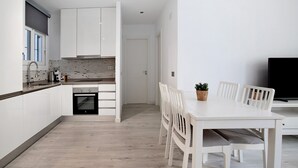 Eine moderne Küche mit weißen Schränken, einem eingebauten Backofen und einem Essbereich mit weißem Tisch und Stühlen.