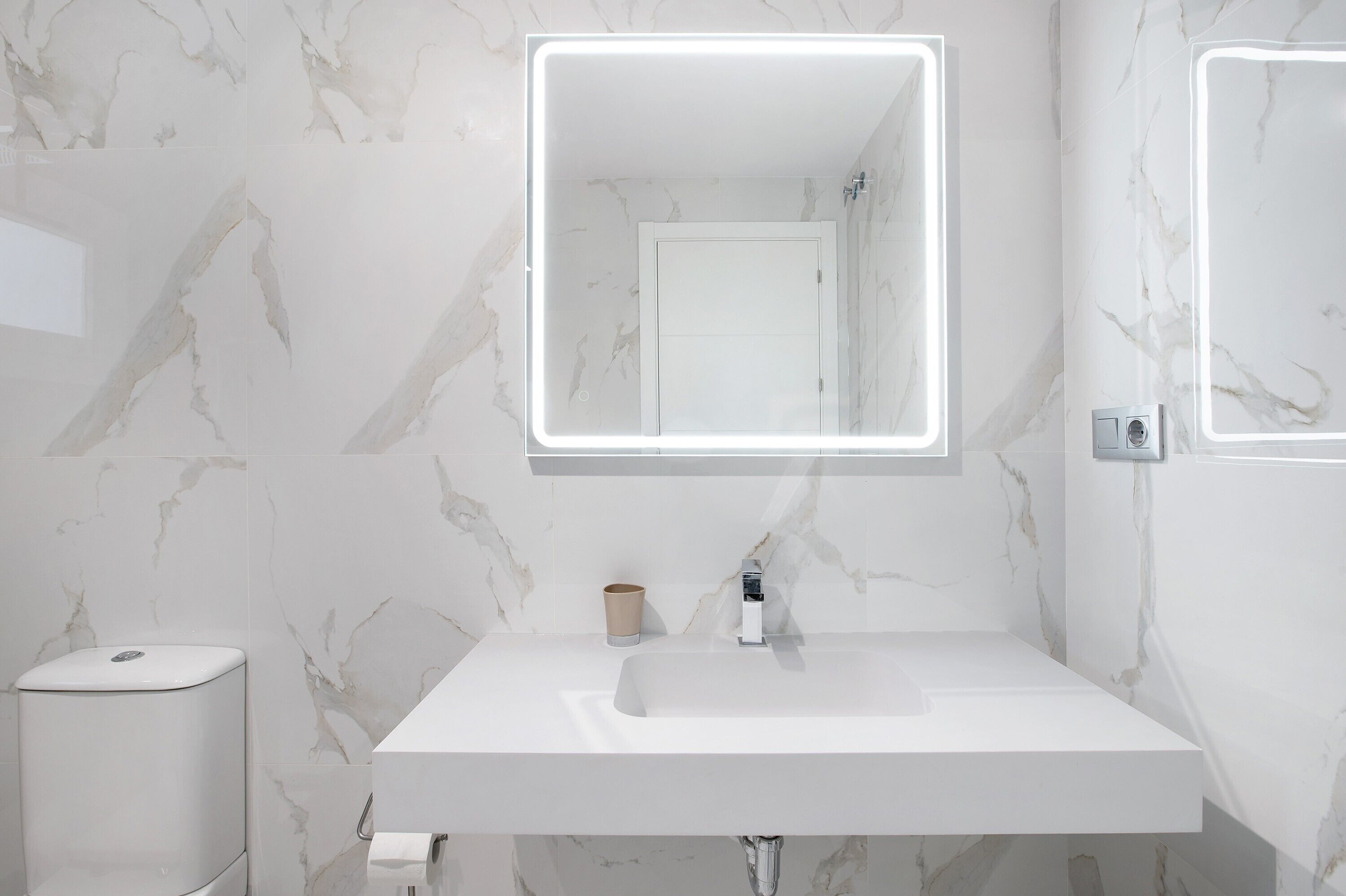 A bathroom with a white sink, marble walls, a mirror, and a toilet.