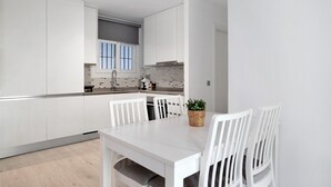 Eine moderne Küche mit weißen Schränken, einem Esstisch mit Stühlen und einem kleinen Blumentopf.