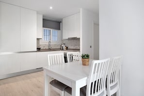 Una cocina moderna con armarios blancos, una mesa de comedor con sillas y una pequeña planta en maceta.