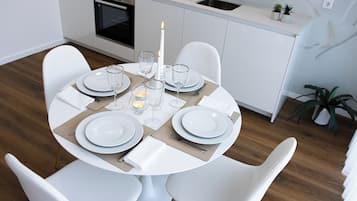 A modern dining area with a round table set for four, white chairs, and a kitchen in the background.