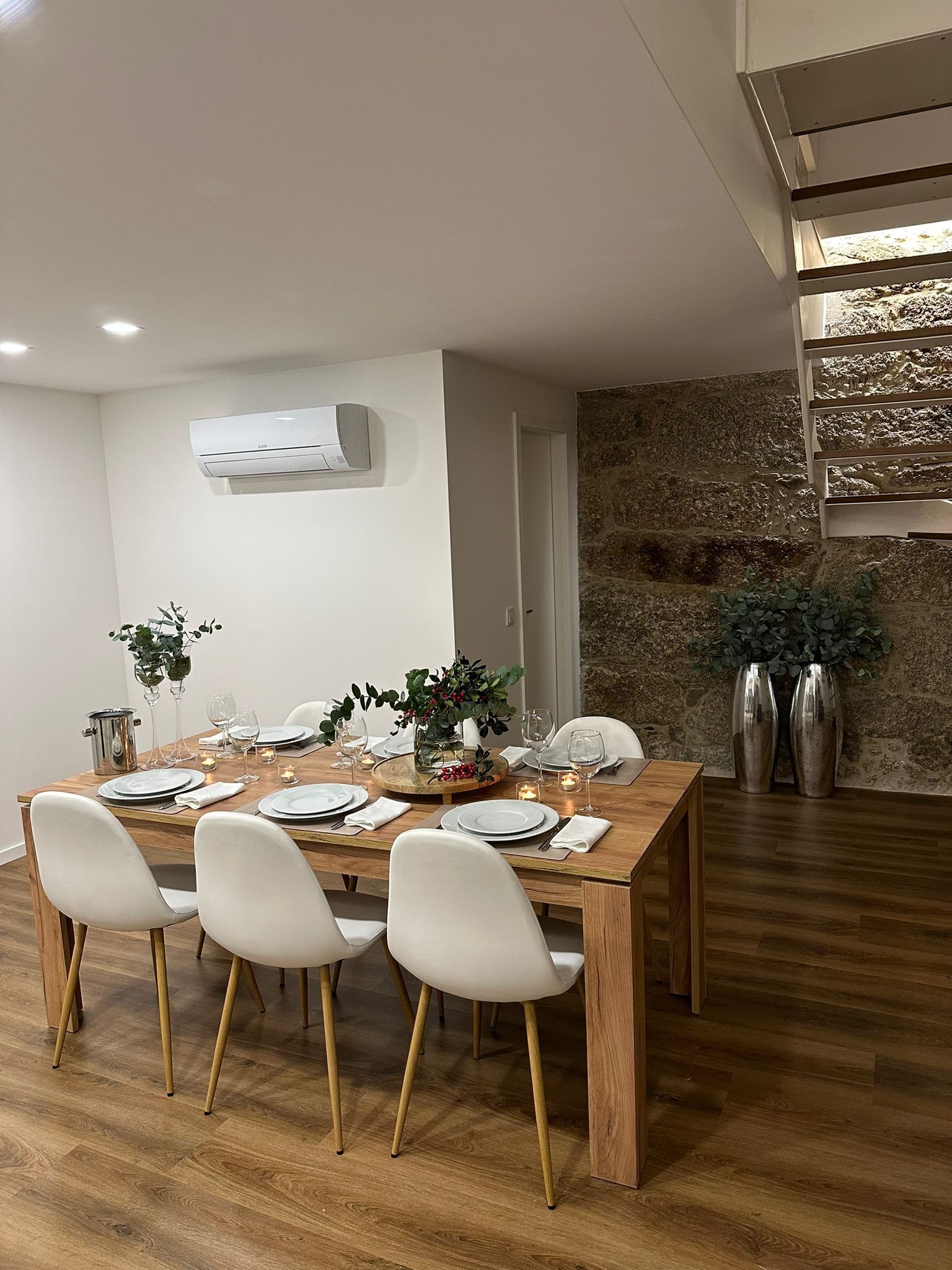 A dining area with a wooden table set for four, white chairs, and a stone wall.