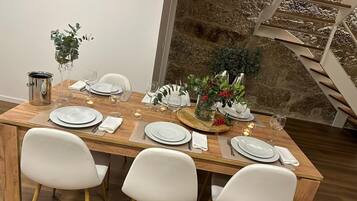 Una mesa de comedor dispuesta con platos blancos, vasos y cubiertos, rodeada de sillas blancas.