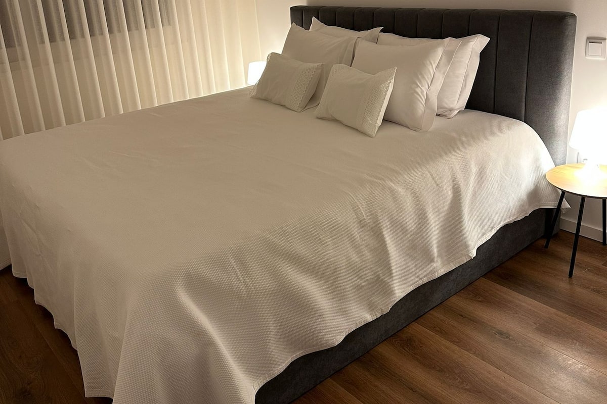 Un grand lit avec une tête de lit sombre, du linge de lit blanc et un plancher en bois.
