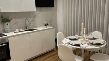 Een moderne keuken met witte kasten, een inbouwoven en een eethoek met een ronde tafel gedekt voor vier personen.