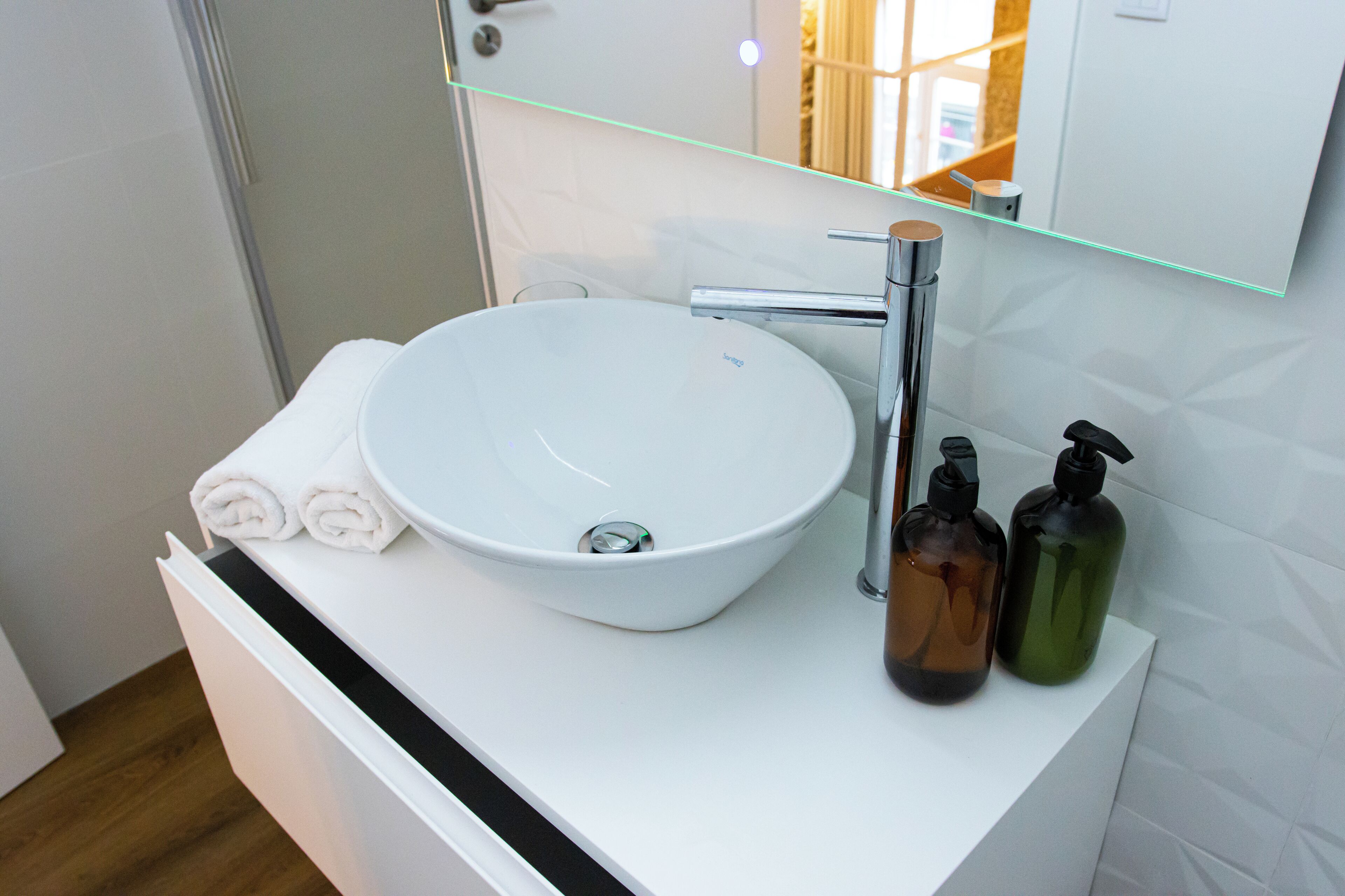 A bathroom with a white sink, a mirror, and two bottles of soap.