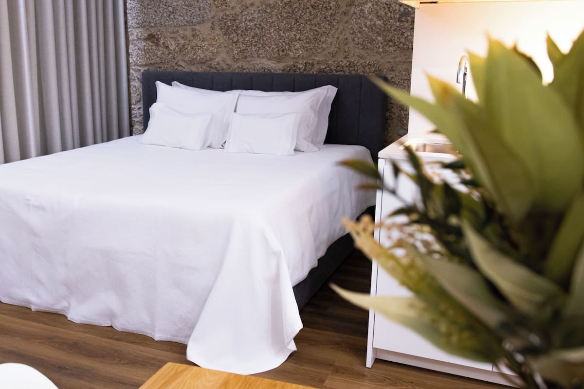 Un lit bien fait, avec du linge de lit blanc, dans une chambre moderne dotée d’un mur en pierre et d’un plancher en bois.