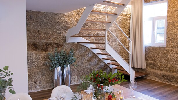 Un comedor con pared de piedra, una escalera blanca y una mesa dispuesta para una comida.
