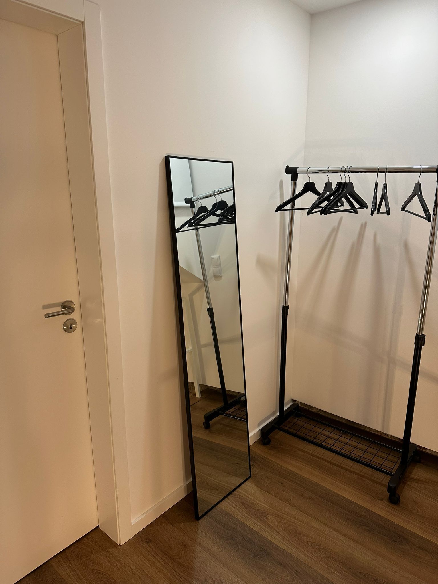 Una habitación con una puerta, un espejo grande y un perchero con ganchos.