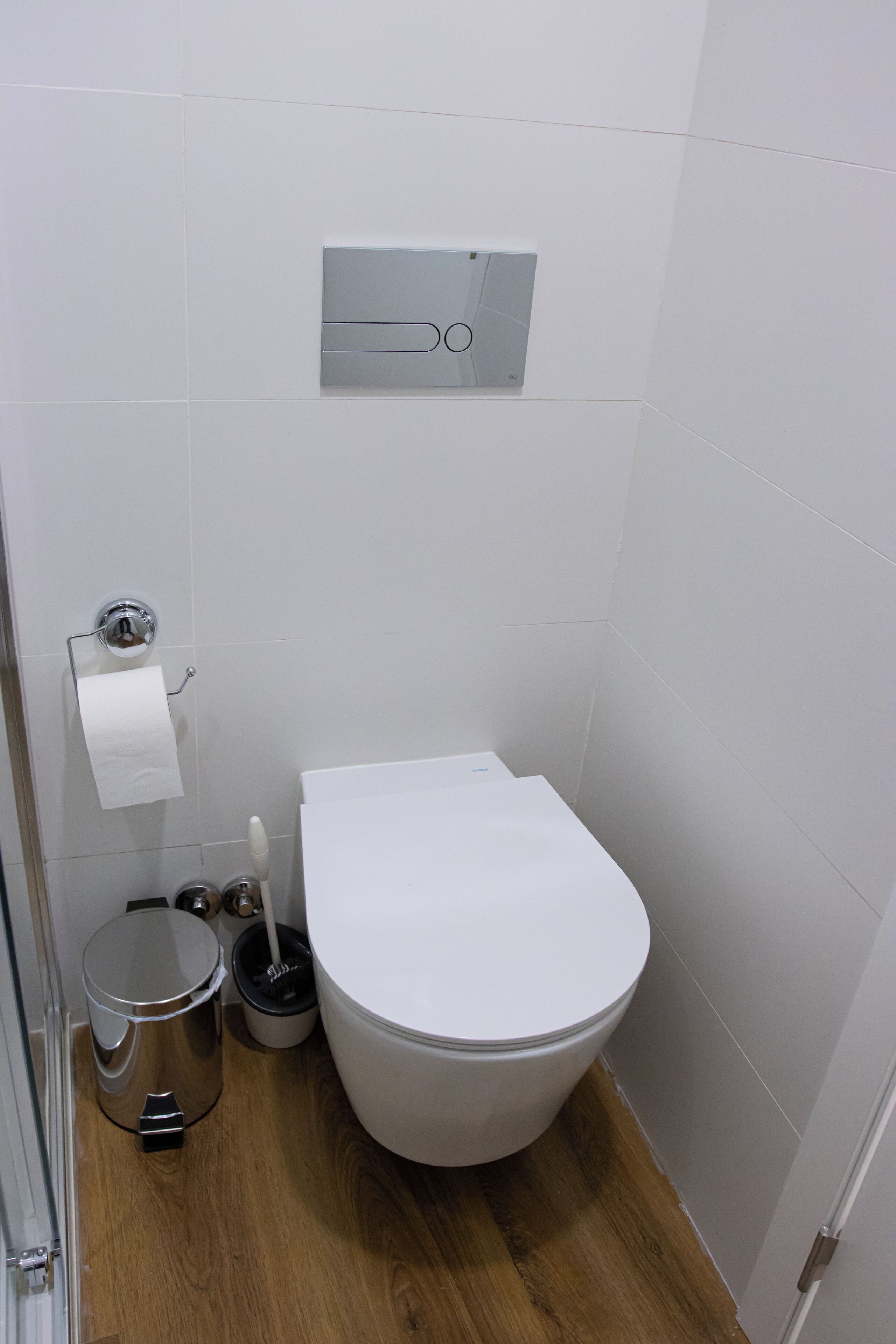 A small, modern bathroom with a white toilet, a trash can, and a toilet paper holder.